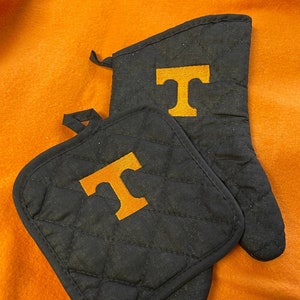 May include: A set of two black quilted oven mitts with a large orange "T" embroidered on each mitt.