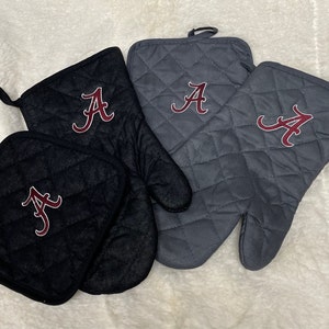 May include: Set of three oven mitts and a pot holder featuring a quilted design. The mitts and pot holder are gray and black with a red embroidered letter "A" on each.