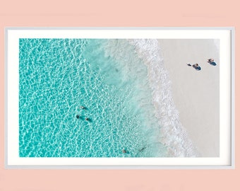 May include: An aerial view of a beach with turquoise water and white sand. The water is clear and shallow, and there are a few people swimming in the water. The sand is white and powdery, and there are a few people walking on the beach.