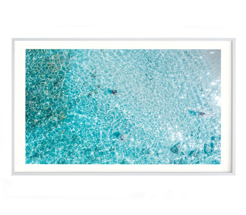 May include: An aerial view of a turquoise blue ocean with ripples and waves. The water is clear and shallow, revealing the sandy bottom.