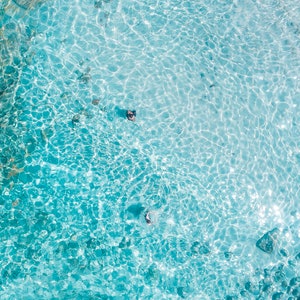 May include: An aerial view of clear, turquoise water with ripples and light reflecting off the surface.  The water is shallow and you can see the bottom.