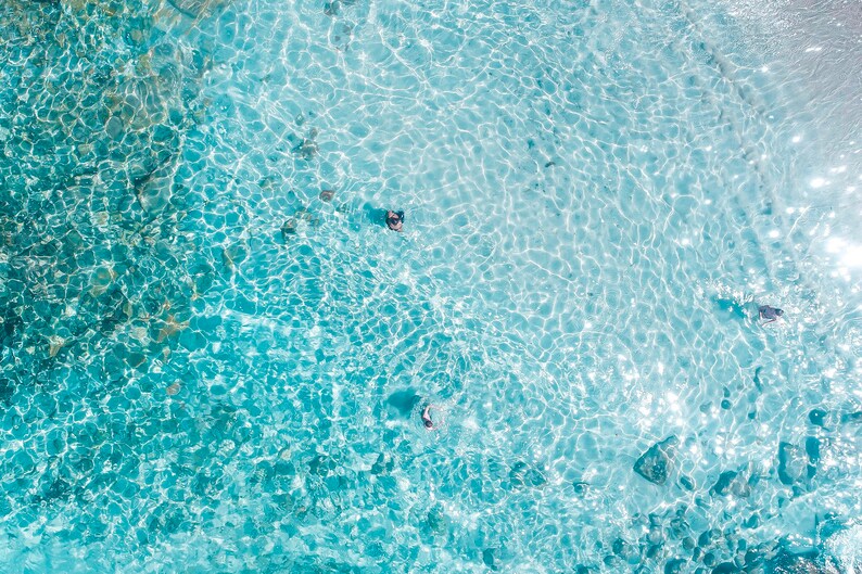 May include: An aerial view of clear, turquoise water with ripples and light reflecting off the surface.  The water is shallow and you can see the bottom.