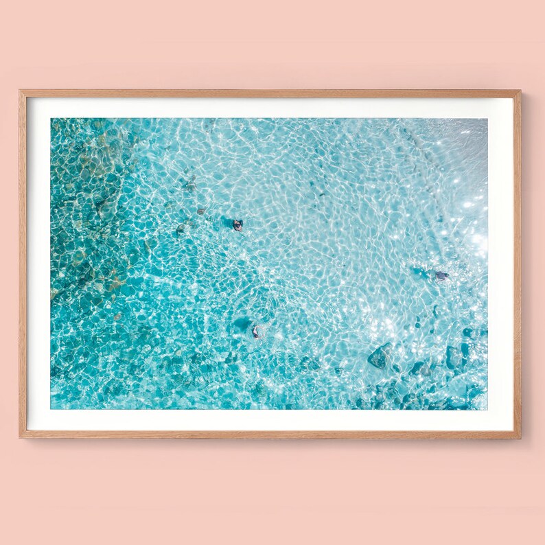 May include: An aerial view of turquoise blue water with ripples and sunlight reflecting on the surface.  Several people are swimming in the water.