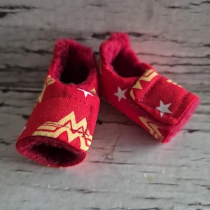 以下が含まれることがあります： 黄色と白の星模様の赤いベビーシューズのペア。靴は柔らかいピンク色の内側とベルクロストラップ留めです。靴は乳児向けに設計されています。