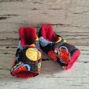 以下が含まれることがあります： カラフルな模様が施された黒い生地のアッパーと、明るい赤色の裏地が特徴のベビーシューズのペア。 円、葉、その他の形がパターン化されています。 乳児向けに設計された靴です。