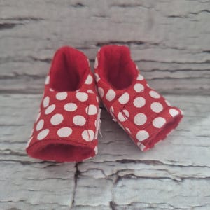 May include: A pair of red baby shoes with white polka dots. The interior of the shoes is red. The shoes are made of fabric and are designed for infants.
