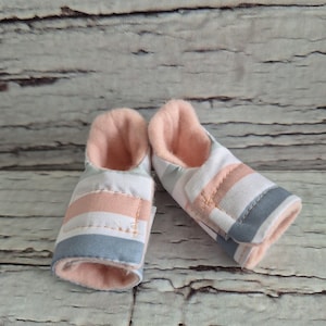 以下が含まれることがあります： 白、薄ピンク、グレーのストライプ柄のベビーシューズのペア。靴の内側はソフトピンクです。スリッパのような構造で設計されています。