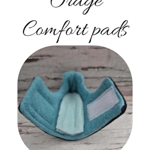 以下が含まれることがあります： 白のベルクロパッチと水色の内装を備えた、ターコイズ色のコンフォートパッド。「Orage Comfort pads」の文字がパッドの上に筆記体で書かれています。