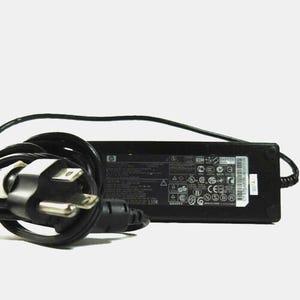 May include: Black HP laptop power adapter with a three-prong plug and a black cord. The adapter has various safety and certification symbols printed on it, along with the HP logo.