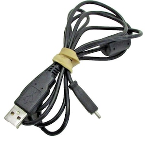 Op de afbeelding: Een zwarte USB-kabel met een standaard rechthoekige connector aan het ene uiteinde en een kleinere, dunne connector aan het andere uiteinde. De kabel is opgerold en vastgezet met een beige elastiekje en bevat een kleine cilindrische ferrietkern.