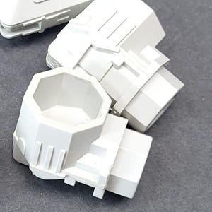 May include: Several white, geometric plastic components, possibly for a larger product. The pieces have a modular design with various shapes, including octagonal and rectangular forms. The components are arranged on a grey surface.