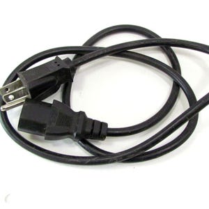 May include: A black power cord with a standard US plug and a C13 connector. The cord is coiled and lies on a white surface. The cord is approximately 6 feet long.