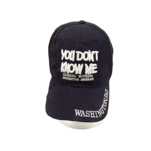 Peut inclure: Casquette de baseball noire avec texte brodé blanc « YOU DON'T KNOW ME » et « FEDERAL WITNESS PROTECTION PROGRAM ». La casquette comporte également « WASHINGTON D.C. » en broderie blanche.
