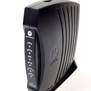 May include: Black Motorola SB5120 SURFboard cable modem. The modem has a series of indicator lights for power, receive, send, online, activity, and standby. The Motorola logo is visible on the front.