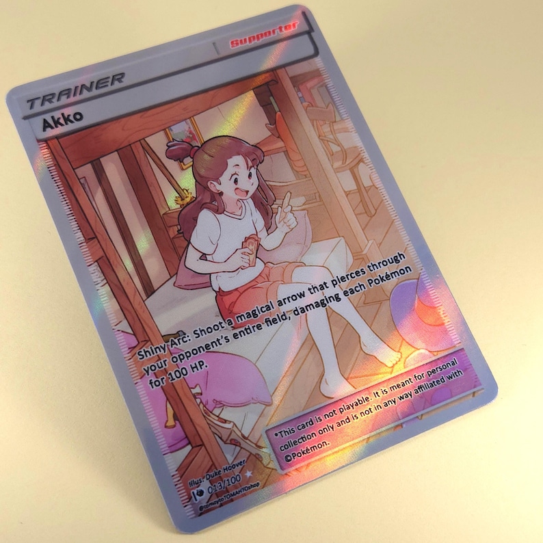 Op de afbeelding: Een Pokemon-verzamelkaartspelkaart met een cartoonillustratie van een meisje met bruin haar en een roze jurk. De kaart heeft de titel "Akko" en de tekst "Shiny Arc: Schiet een magische pijl die door het hele veld van je tegenstander gaat en elk Pokemon 100 schade toebrengt." De kaart is een ondersteuningskaart.