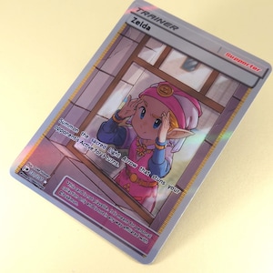 May include: A Pokemon Trainer card featuring Zelda, a character from the Legend of Zelda video game series. The card is a supporter card and has the text "Summon the sacred Light Arrow that stuns your opponent's Active for 3 turns."