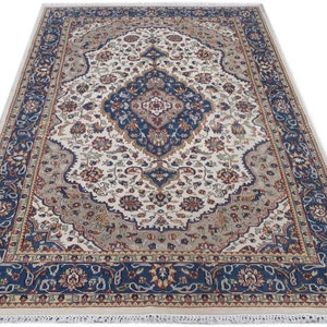 Puede incluir: Una alfombra de color crema con un patr&oacute;n floral azul y rojo. La alfombra tiene un medall&oacute;n central con un dise&ntilde;o azul y blanco. La alfombra tiene un borde de flecos.