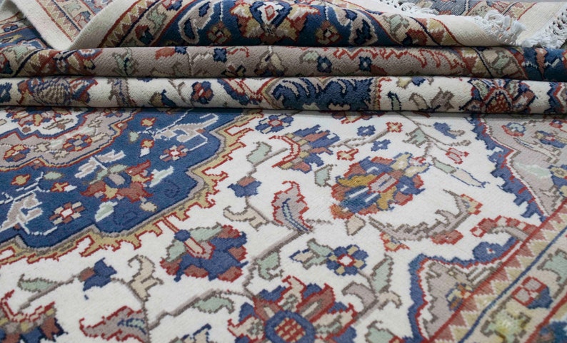 Puede incluir: Una alfombra blanca con un patr&oacute;n floral azul, rojo y dorado. La alfombra est&aacute; doblada en tres partes, mostrando los intrincados detalles del dise&ntilde;o.