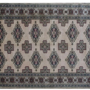 Puede incluir: Una alfombra beige con un patrón repetitivo de formas geométricas azul oscuro, negro y rosa. La alfombra tiene un borde de flecos.