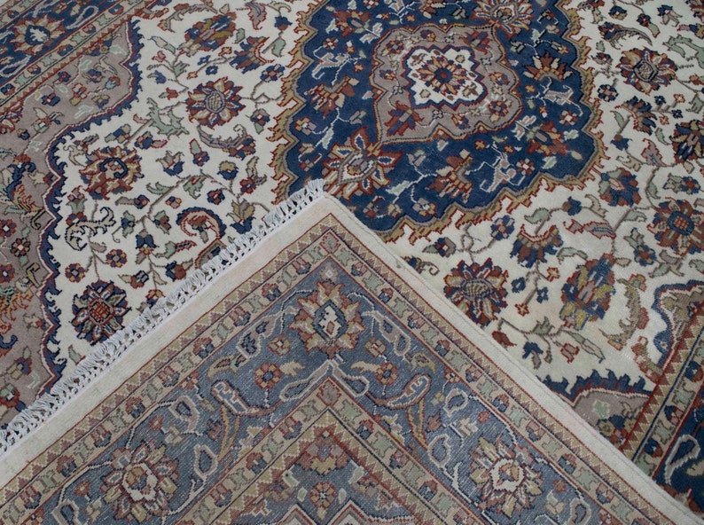 Puede incluir: Una alfombra de color crema con un patr&oacute;n floral azul y rojo. La alfombra tiene un borde de flecos.