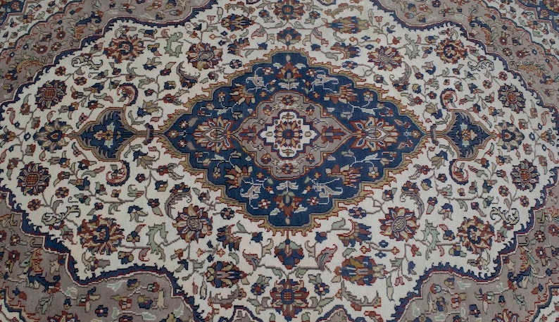 Puede incluir: Una alfombra de color crema con un dise&ntilde;o detallado e intrincado en tonos de azul, marr&oacute;n y rojo. La alfombra presenta un medall&oacute;n central con forma de diamante y motivos florales.