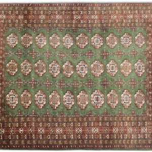 Puede incluir: Una alfombra verde con un diseño persa tradicional. La alfombra tiene un medallón central con detalles intrincados y un borde con patrones repetitivos. Los colores son apagados y terrosos, con tonos de verde, marrón y crema.