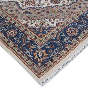 Puede incluir: Primer plano de la esquina de una alfombra de color crema con un patr&oacute;n floral azul, rojo y verde. La alfombra tiene un borde de flecos blancos.