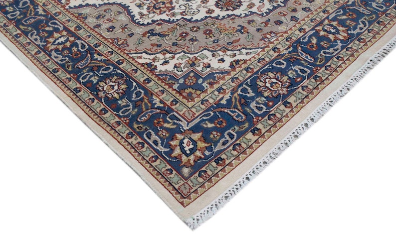 Puede incluir: Primer plano de la esquina de una alfombra de color crema con un patr&oacute;n floral azul, rojo y verde. La alfombra tiene un borde de flecos blancos.