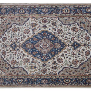 Puede incluir: Una alfombra persa tradicional con fondo crema y intrincados patrones florales azules, rojos y beige. La alfombra tiene un borde con un dise&ntilde;o floral repetitivo.