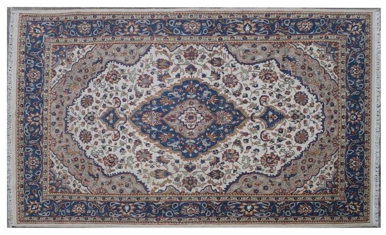 Puede incluir: Una alfombra persa tradicional con fondo crema y intrincados patrones florales azules, rojos y beige. La alfombra tiene un borde con un dise&ntilde;o floral repetitivo.