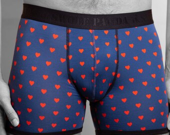 May include: Blue boxer briefs with a pattern of red hearts. The waistband is black with the text "WOLF PANDA" printed on it. The briefs have black trim around the legs.