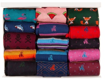 May include: A white box filled with rolled-up socks. The socks feature various patterns, including flamingos, watermelons, foxes, sharks, skulls, and geometric designs. Colors include teal, pink, green, red, and navy. Each sock has a small embroidered logo.