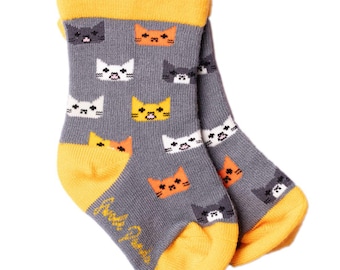 May include: A pair of gray socks with a repeating pattern of cat faces in white, orange, yellow, and gray. The toe and cuff are yellow. The text "Uncle Paulie's" is printed on the side of the sock.
