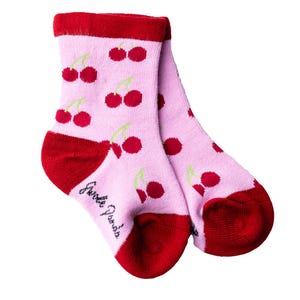 May include: A pair of pink socks with a red cherry print. The socks have red cuffs and the words "Little Giraffes" are printed on the bottom of one sock.