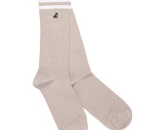 May include: A pair of beige ribbed socks with white stripes at the top. A small black gorilla logo is embroidered below the stripes. The socks are made of a soft, comfortable material.