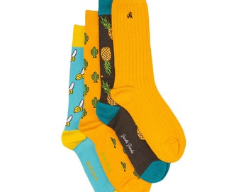 May include: A set of four colorful socks with different patterns. The socks feature pineapples, bananas, and cacti. The socks are yellow, blue, green, and brown.