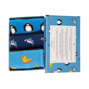 May include: A gift box set of three pairs of socks with fun animal designs. One pair features penguins, another sharks, and the third has yellow ducks. The box and socks are shades of blue.