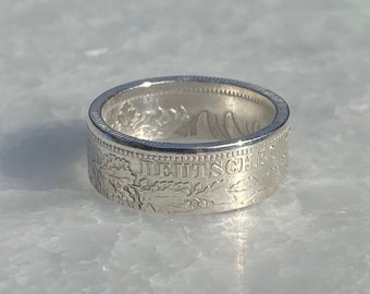 Könnte beinhalten: Ein silberner Ring aus einer deutschen Münze. Die Münze trägt die Aufschrift "DEUTSCHE" und ein florales Design.
