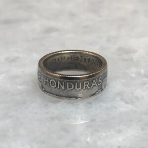 Puede incluir: Un anillo de plata hecho con una moneda hondureña de 50 centavos. El anillo está grabado con "50 CENTAVOS DE HONDURAS".