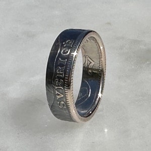 Könnte beinhalten: Ein silberner Ring aus einer wiederverwendeten Münze. Der Ring trägt die Inschrift "SVENSKA" an der Seite.