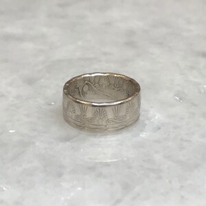 May include: A silver ring with an intricate design of stylized waves and floral patterns.