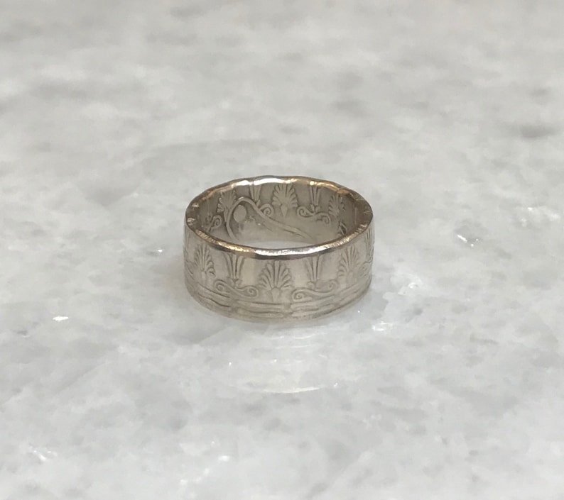 May include: A silver ring with an intricate design of stylized waves and floral patterns.