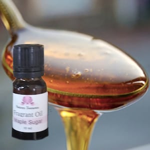 May include: A small brown glass bottle with a black cap, labelled "Fragrant Oil Maple Sugar" with a pink floral logo. The background shows a blurred image of a spoon with a golden liquid, possibly syrup, dripping from it. The bottle contains 10 ml of oil.