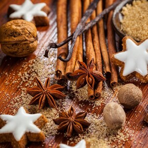 May include: A close-up of various baking spices, including cinnamon sticks, star anise, and nutmeg, arranged on a wooden surface with brown sugar and a walnut.