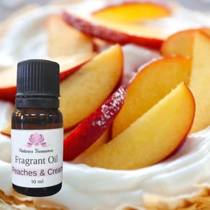 May include: A small brown glass bottle with a black cap. The bottle contains a fragrant oil called "Peaches & Cream" by Natures Treasures. The bottle is 10 ml. The background is a close-up of sliced peaches on a white surface.