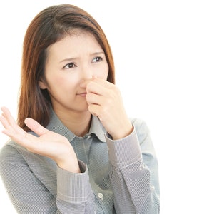 May include: A woman with brown hair is holding her nose with her right hand and looking to the side. She is wearing a grey and white striped shirt.