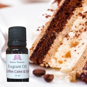 May include: A small brown glass bottle with a black cap. The bottle contains a fragrant oil called "Coffee Cake & Spice" by "Natures Treasures". The bottle is labelled with a pink flower logo and contains 10 ml of oil. A slice of coffee cake with white frosting and chocolate layers is in the background.