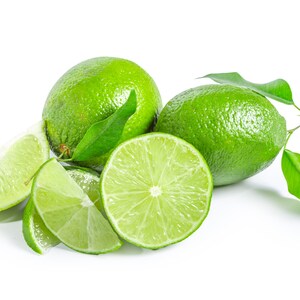 May include: A group of limes, some whole and some cut into wedges, with green leaves. The limes are a bright green colour and the leaves are a darker green.