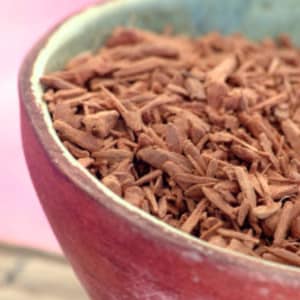 May include: Close-up of a bowl filled with loose, reddish-brown sandalwood chips.