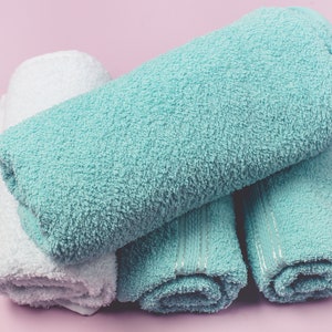 May include: A stack of four towels, two white and two light blue, folded and rolled up. The towels are soft and fluffy, ideal for drying off after a bath or shower.